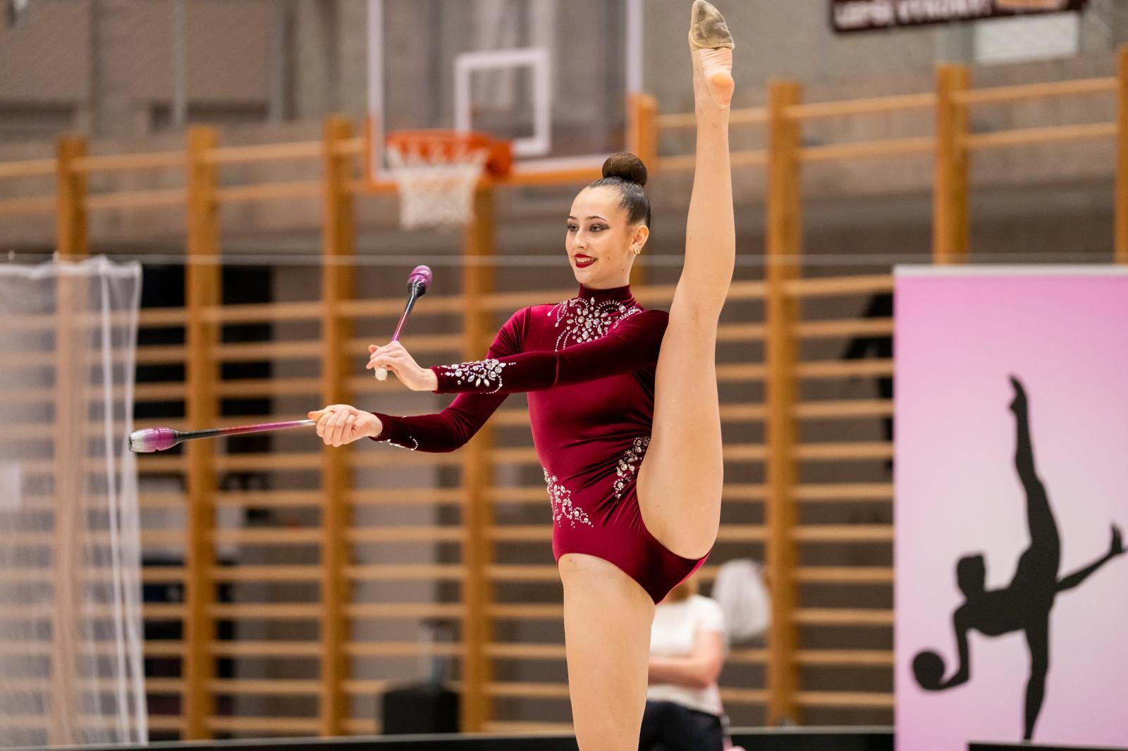 Gymnastka v bordó dresu drží rovnováhu s kužely