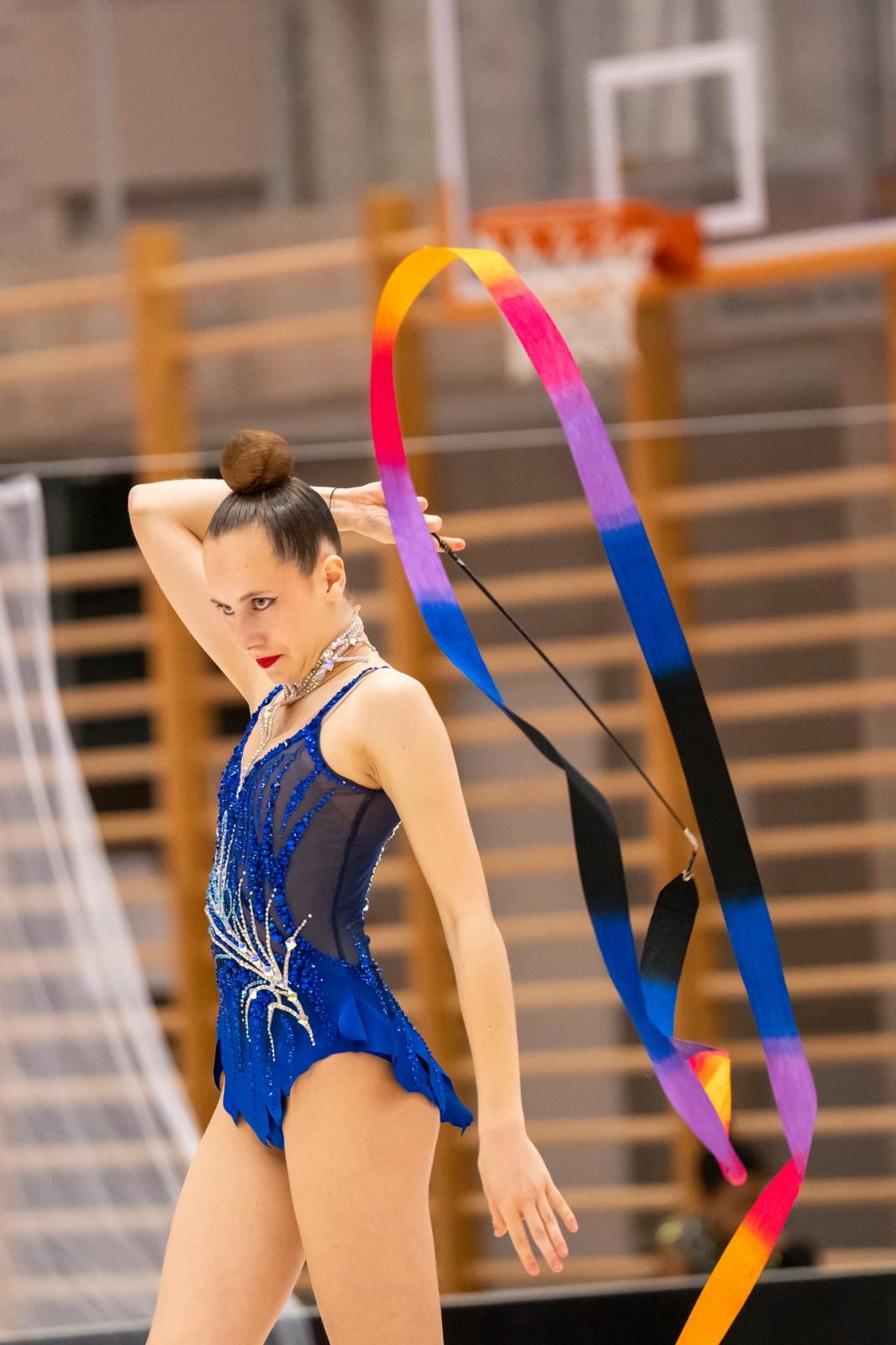 Gymnastka v modrém dresu cvičí se stuhou